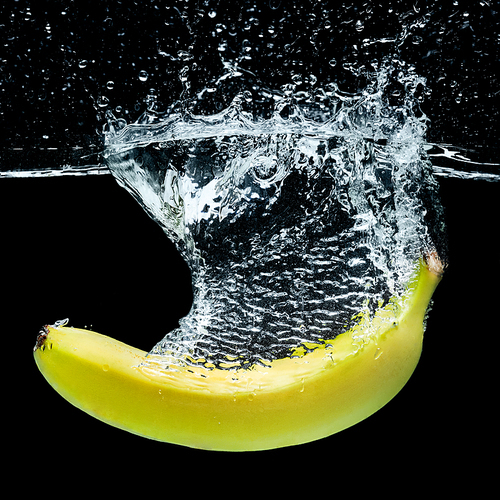 close up view of banana in water with splashes isolated on black
