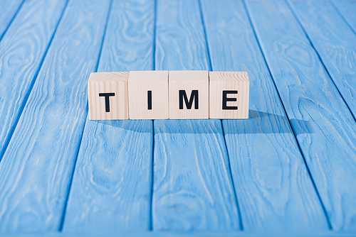 close up view of time word made of wooden cubes on blue surface