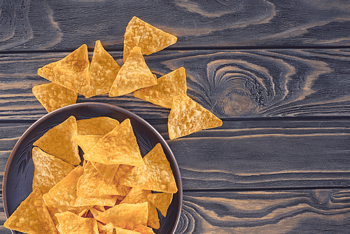 top view of crispy unhealthy nachos in bowl on wooden table