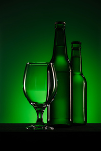 close up view of bottles of beer and empty glass on green background