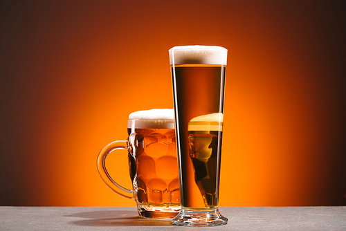 close up view of arrangement of glasses of beer with froth on orange backdrop
