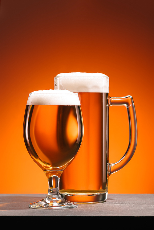 close up view of arrangement of glasses of beer with foam on orange backdrop