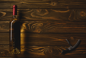 top view of bottle of white wine and corkscrew on wooden table