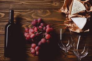 top view of bottle of red wine with glasses and appetizers on wooden table