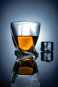 glass with whiskey and ice cube with reflection, on dark grey background