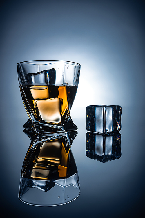 glass with cognac and ice cubes with reflections, on dark grey background