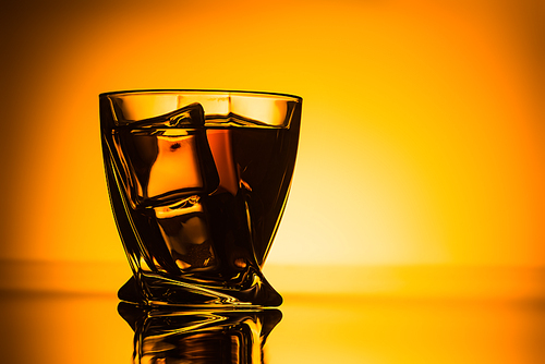 silhouette of glass with cognac and ice cubes on orange background