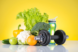 close-up view of dumbbell, bottle of water and fresh fruits and vegetables on yellow