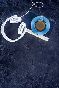 top view of book, white headphones and blue cup with coffee on grey tabletop