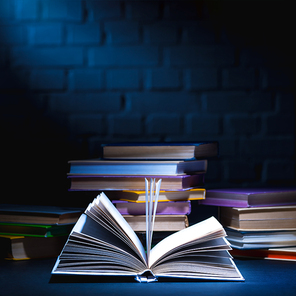 open book in front of stack of colored books on dark surface