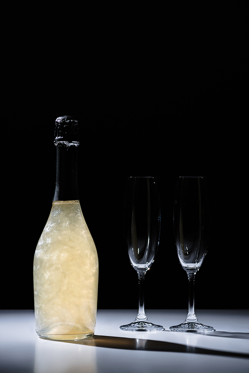 close up view of bottle of champagne and empty glasses on black background