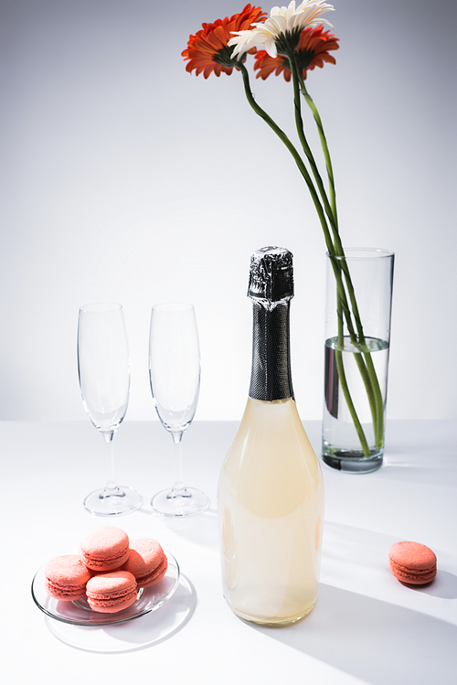유토이미지 | close up view of macarons, empty glasses, bottle of champagne and bouquet of gerbera flowers on grey backdrop