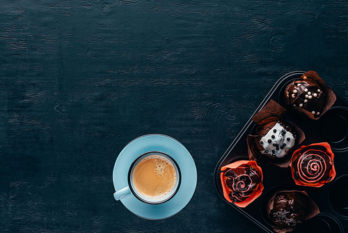 Top view of delicious muffins with glaze and blue cup of coffee on wooden background