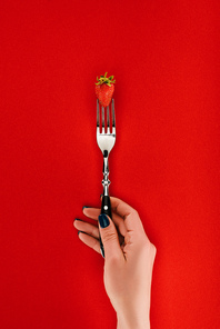 Female hand holding fork with strawberry isolated on red background