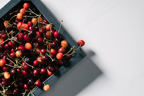 top view of fresh ripe sweet cherries in wooden box on white