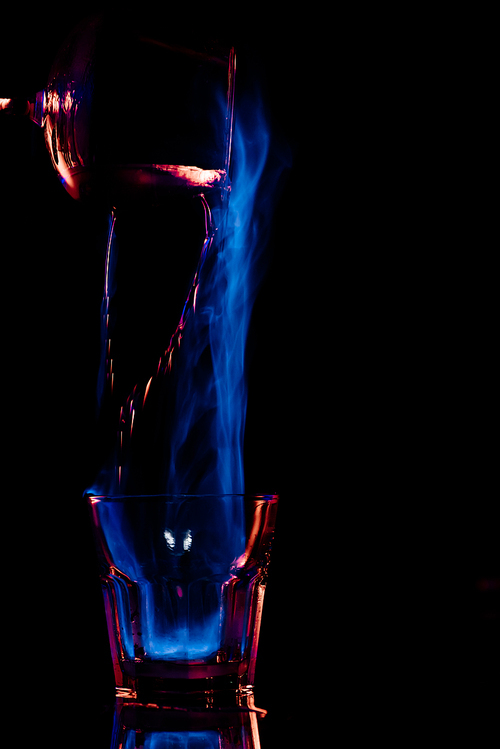 close up view of pouring burning sambuca alcohol drink into glass process on black background