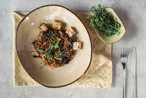 food composition with sprouts in bowl, soba with tofu and vegetables decorated with germinated seeds of sunflower on grey tabletop