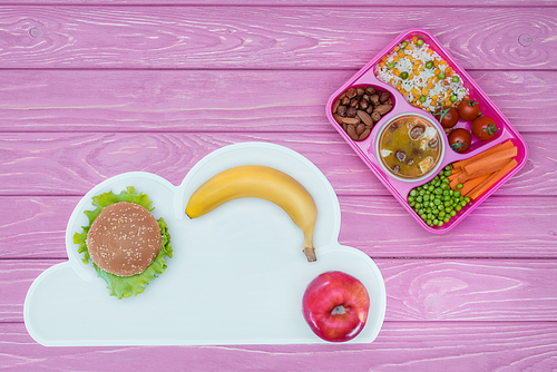 top view of tray with kids lunch for school, burger and fruits on pink tabletop