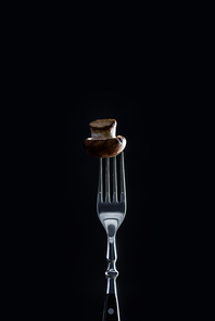 raw champignon mushroom on fork isolated on black