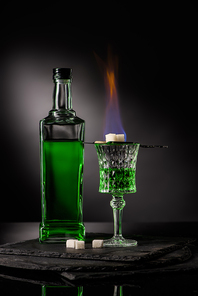 close-up shot of spoon with sugar cubes over burning absinthe in glass on dark background