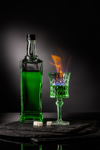 close-up shot of bottle and glass of burning absinthe on dark background