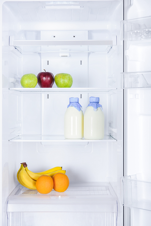 ripe tasty apples, bananas, oranges and bottles of milk in fridge
