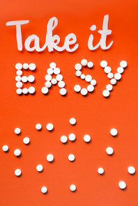 top view of lettering take it easy by white pills on red background