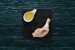 top view of chicken leg with pepper corns and oil on stone board