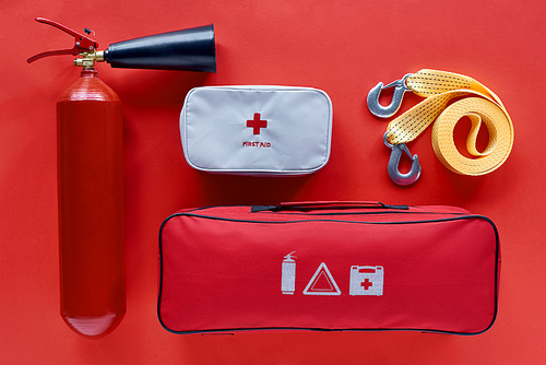 flat lay with fire extinguisher, automotive handbag, first aid kit and car tow rope on red backdrop