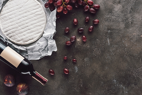 top view of bottle of wine, brie cheese, figs and grape on dark surface