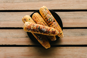 top view of delicious grilled salted corn on plate on wooden table