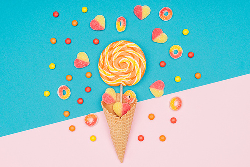 top view of jelly candies, lollipop and waffle cone on blue and pink surface