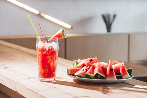 close up view of refreshing watermelon drink in glass and pieces of fresh watermelon on wooden surface in cafe