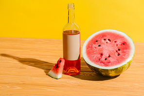 close up view of fresh watermelon and watermelon drink in bottle on wooden surface on yellow background
