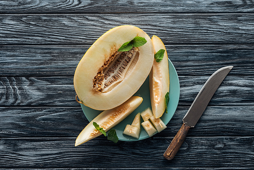 top view of sweet ripe sliced melon with mint on plate and knife on wooden surface