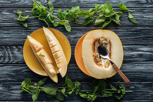 top view of fresh ripe sweet melon with spoon and fresh mint on wooden surface