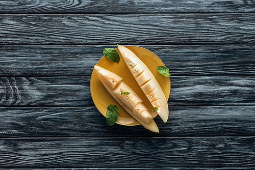 top view of fresh ripe sweet sliced melon on yellow plate on wooden surface