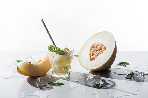 summer drink with mint and melon in glass, melted ice cubes and sweet ripe melon on white
