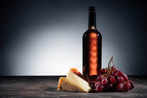 bottle of red wine, different types of cheeses and grapes on wooden table