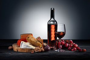 bottle of red wine, wineglass and different types of cheeses on grey