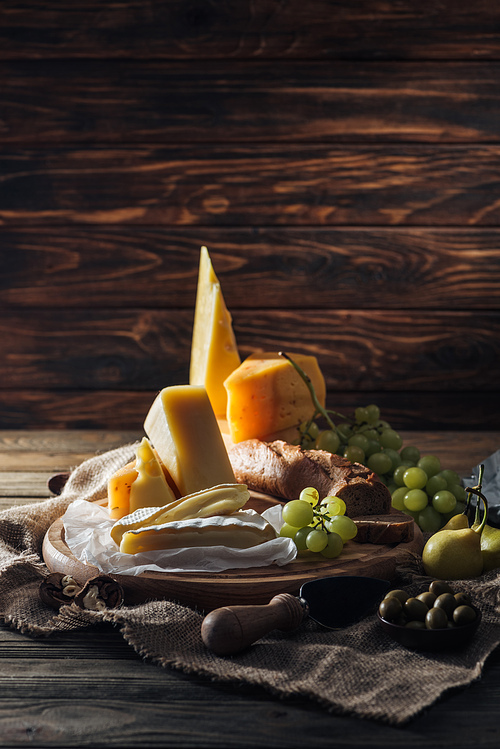 tasty different types of cheeses, grapes and pears on table in kitchen