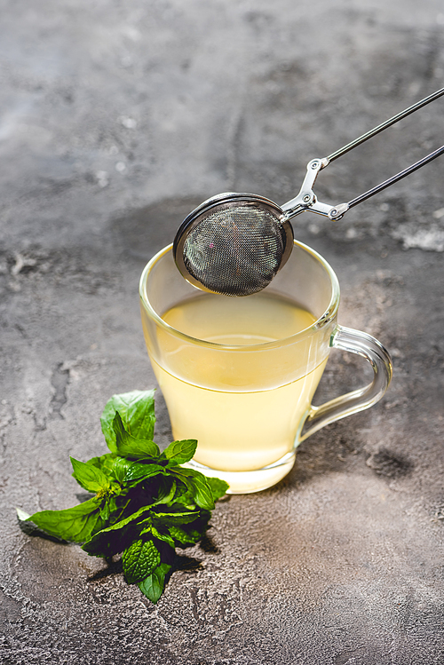 healthy tea with mint and tea strainer on grey surface