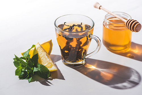 healthy black tea with honey, lemon and mint in cup on white tabletop