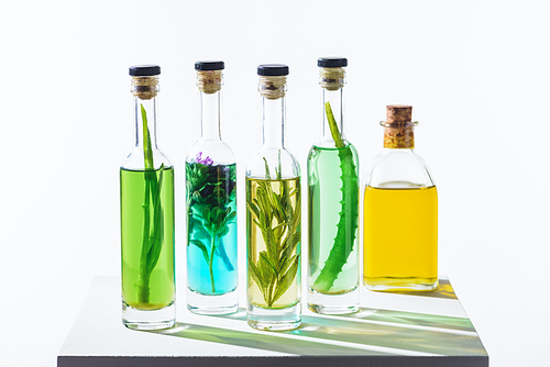 bottles of aromatic essential green and yellow oils with herbs on white cube