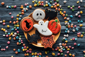 top view of plate with halloween cookies surrounded by colorful candies on wooden table