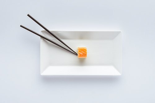 top view of delicious sushi with salmon and chopsticks on white plate isolated on white