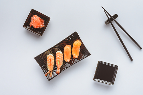 top view of tasty sushi with salmon and shrimp, ginger and chopsticks isolated on white