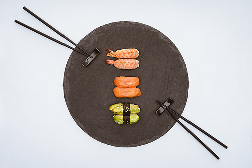 top view of delicious sushi on slate board and chopsticks isolated on white