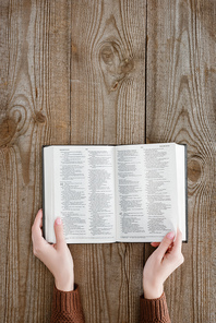 cropped shot of woman holding opened holy bible on wooden tabletop