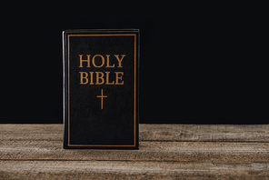 close-up shot of holy bible standing on wooden table isolated on black